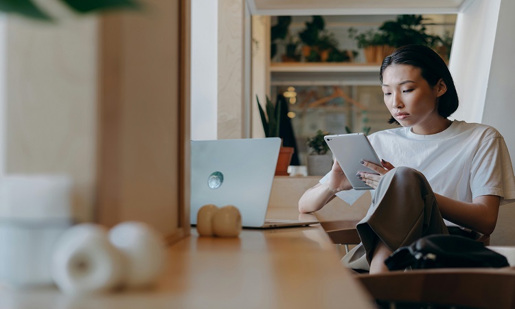 Woman sitting at a desk working on a tablet with a computer in front of her.