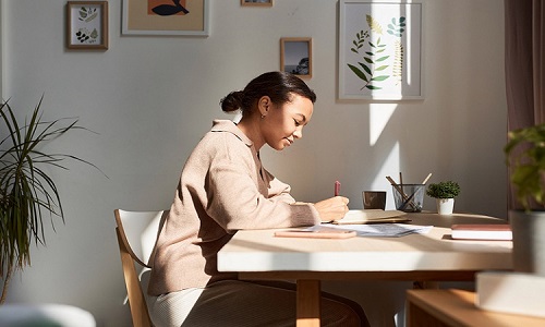 Minimal side view portrait of young woman writing in notebook at home with sun rays, copy space