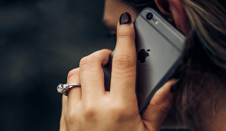 Women talking on gray iphone with painted nails wearing a diamond ring.
