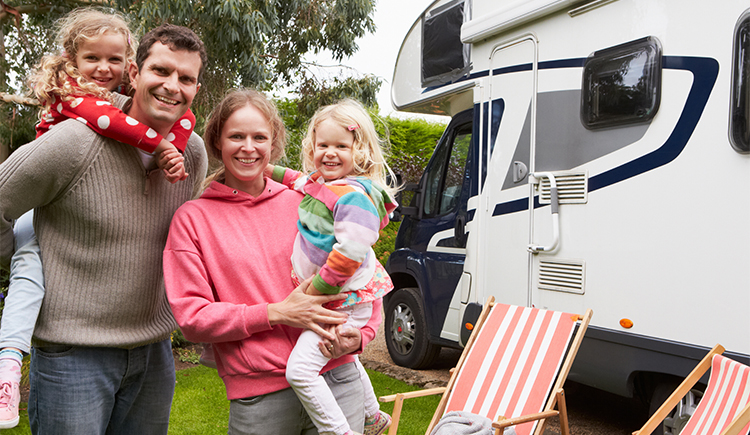 Woman in a pink sweatshirt posing for a photo while holding a little girl smiling in front of an RV