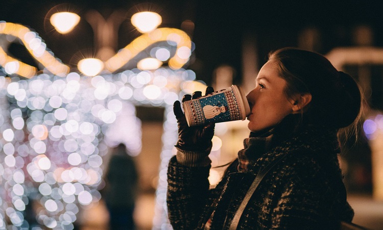 Woman drinking out of snowman coffee cup looking at holiday lights in winter