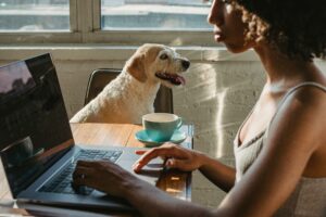 Woman typing on laptop next to a small dog and coffee mug.