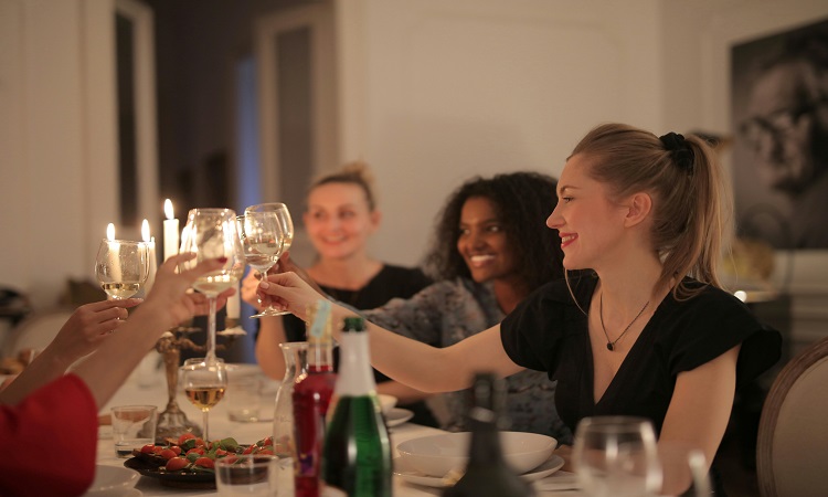 Women toasting wine glasses at candlelit dinner party.