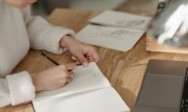 woman writing in notebook on a desk.