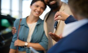 Close up of couple taking keys from a salesperson after buying new car in showroom.