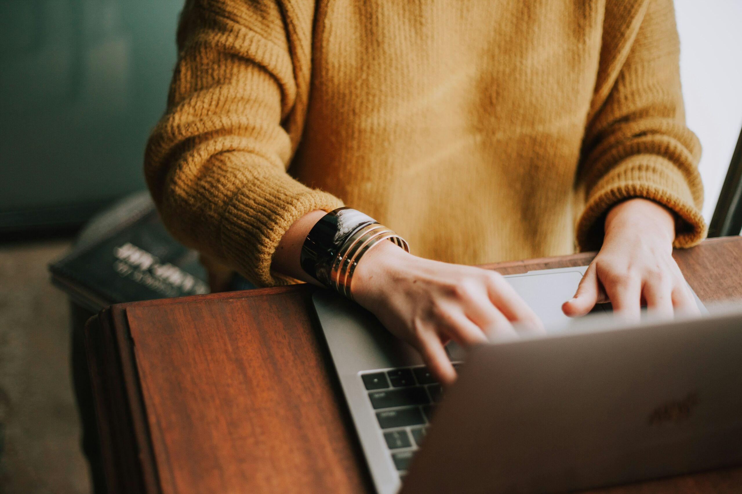 Woman wearing a yellow sweater typing on a laptop.