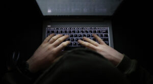 Person with a hoody typing at a computer in the dark suspicious online behavior