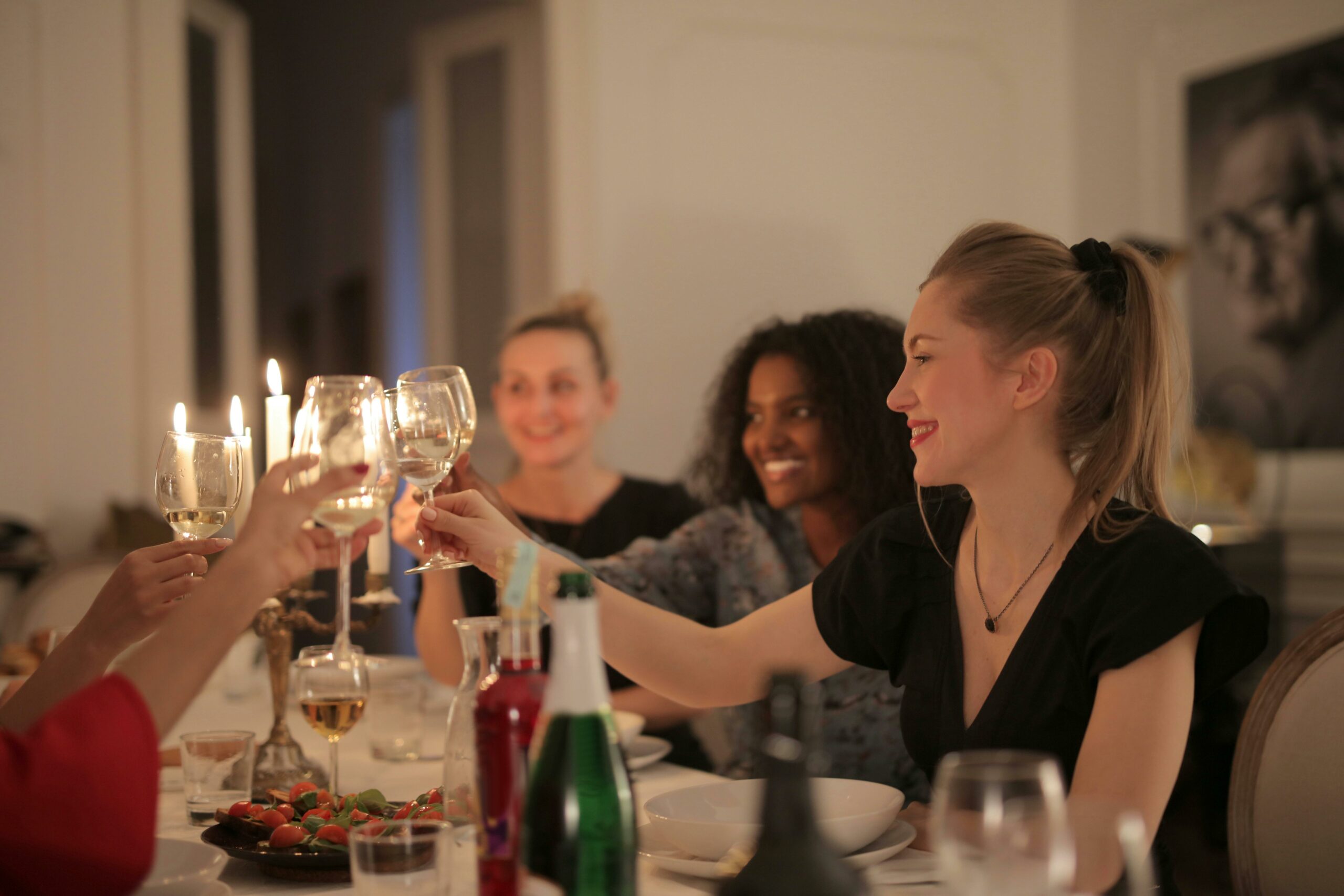 Women at a dinner party drinking wine and smiling near candlelight.
