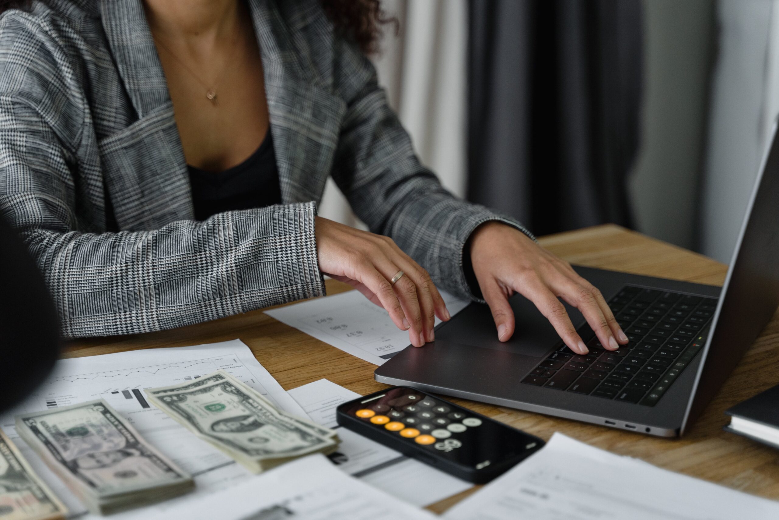 Women budgeting on laptop with calculator and cash in front of her.