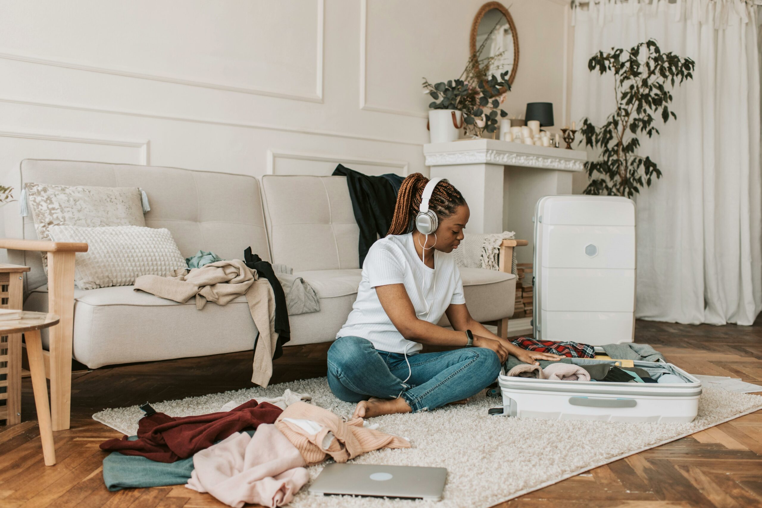 Financial Literacy blog featuring a woman sitting on floor packing clothes into a suitcase white listening to a podcast.